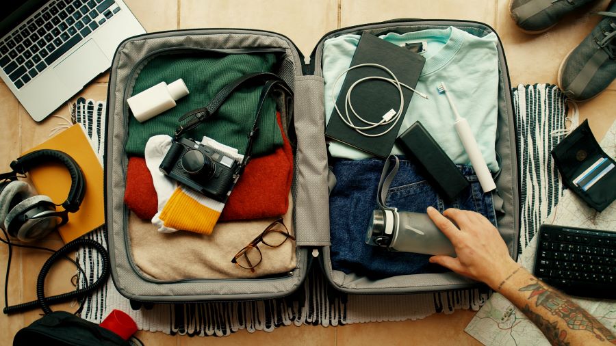 Man packs his bag for travel and includes thing like a camera and electric toothbrush.